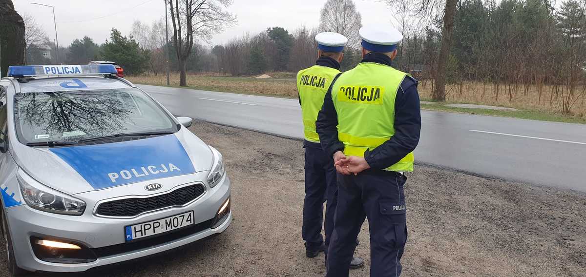 Policyjny patrol stoi na drodze obok radiowozu i czuwa nad bezpieczeństwem