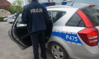 Policjant przy radiowozie w którym jest zatrzymany złodziej