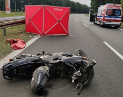 Miejsce zdarzenia drogowego-motocykl leży na drodze, w tle karetka pogotowia i rozłożony parawan ochronny