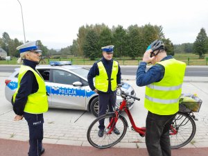 Policjanci rozmawiają z rowerzystą, który zakłada na głowę kask ochronny