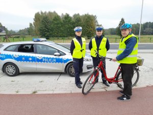 Wspólne zdjęcie policjantów i rowerzysty ubranego w kask i kamizelkę odblaskową