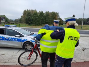 Policjantka zakłada kamizelkę rowerzyście- w tle radiowóz policyjny