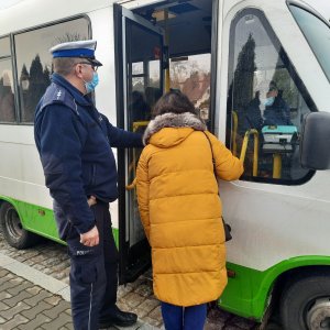 Policjant i kobieta stoją przed wejściem do busa- rozmawiają z kierowcą