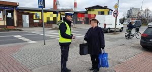 Policjant rozmawia z kobietą -wręcza jej opaskę odblaskową