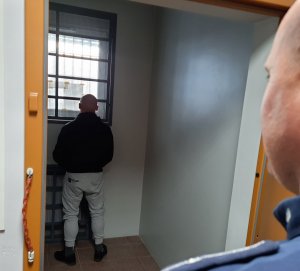 Policjant kontroluje pokój przejściowy w którym zamknięty jest zatrzymany
