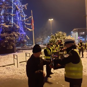 Policjantka wręcza odblask pieszemu- w tle choinka świąteczna