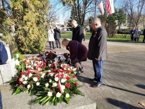 Delegacja dwóch mężczyzn i kobieta składają kwiaty pod pomnikiem