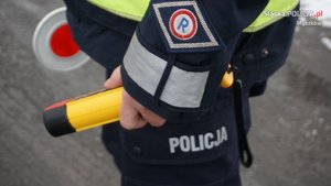 Policjant trzyma urządzenie do badania stanu trzeźwości i tarczę służącą do zatrzymywania pojazdów