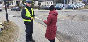 Policjant rozmawia z pieszą i przekazuje jej odblaskową opaskę