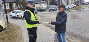 Policjant rozmawia z pieszym, któremu przekazuje opaskę odblaskową