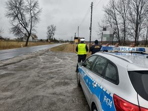 Patrol mundurowych stoi przy radiowozie i obserwuje drogę