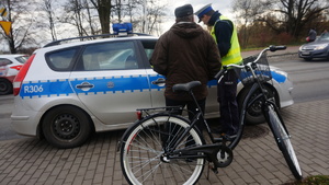 Policjant kontroluje rowerzystę. W tle policyjny radiowóz