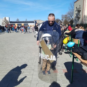 Policjant pomaga dziecku ubrać policyjny sprzęt