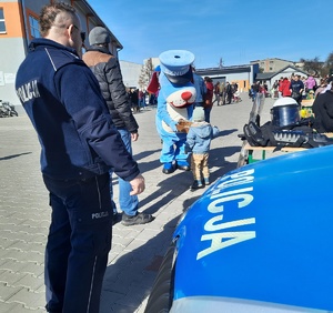 Sznupek częstuje cukierkami dziecko- obok stoi policjant przy radiowozie