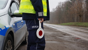 Policjant stoi przy drodze i trzyma tarczę do zatrzymywania pojazdów