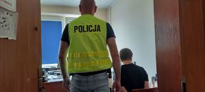 Policjant stoi za mężczyzną który siedzi na stołku