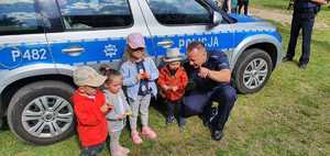 Policjant z dziećmi pozuje do zdjęcia przy radiowozie