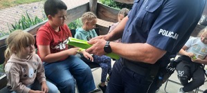 Policjant wręcza opaski odblaskowe dzieciom