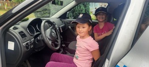 Dwie dziewczynki w policyjnych czapkach siedzą w radiowozie