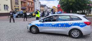 Motocykliści na trasie przejazdu, którą zabezpiecza policjant stojący przy radiowozie