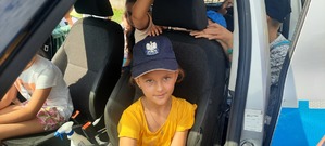 Dziecko w policyjnej czapce siedzi w radiowozie za kierownicą