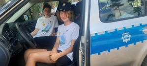 Dziewczynka w policyjnej czapce siedzi za kierownicą radiowozu