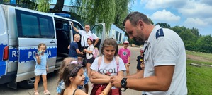 Dzieci zwiedzają radiowóz policyjny i przymierzają kajdanki