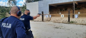 Policjant strzela do tarczy- za nim stoi instruktor