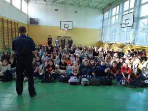 Policjant mówi do dzieci siedzących w hali gimnastycznej
