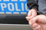 Kajdanki założone na ręce trzymane z tyłu- w tle napis Policja