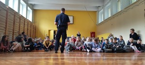 Dzieci siedzą na podłodze i słuchają tego co mówi policjant