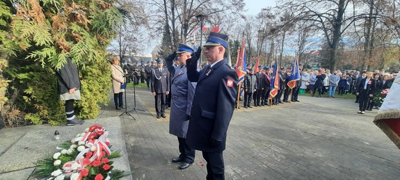 Policjant i strażak oddają honor przed pomnikiem