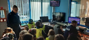 Policjant i dzieci w pomieszczeniu służbowym z monitorami i telefonami