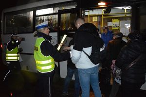 Mundurowi wręczaja odblaski pasażerom wysiadającym z autobusu miejskiego