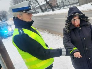 Policjantka zakłada opaskę odblaskową na rękaw  pieszej