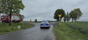 Zdjęcie radiowozu policyjnego, w tle widać wóz strażacki, umundurowanego policjanta i strażaków