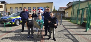 Na zdjęciu widać umundurowanych policjantów, dzieci, maskotkę sznupka a w tle radiowozy