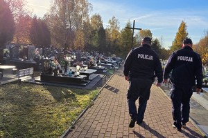 Na zdjęciu widać dwóch policjantów idących po cmentarzu