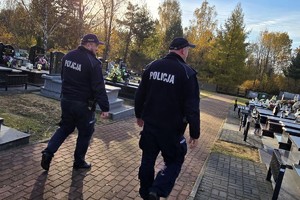 Na zdjęciu widać dwóch policjantów idących po cmentarzu