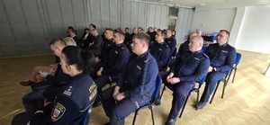 Na zdjęciu widzimy policjantów siedzących patrzących na wyświetlaną prezentację