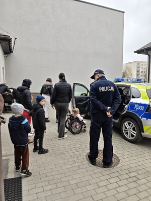 Zdjęcie przedstawia policjanta z dziećmi stojących przy radiowozie.