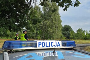 Na zdjęciu widać koguty policyjne na samochodzie i stojących policjantów