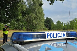 Na zdjęciu widać koguty policyjne na samochodzie i stojącego policjanta